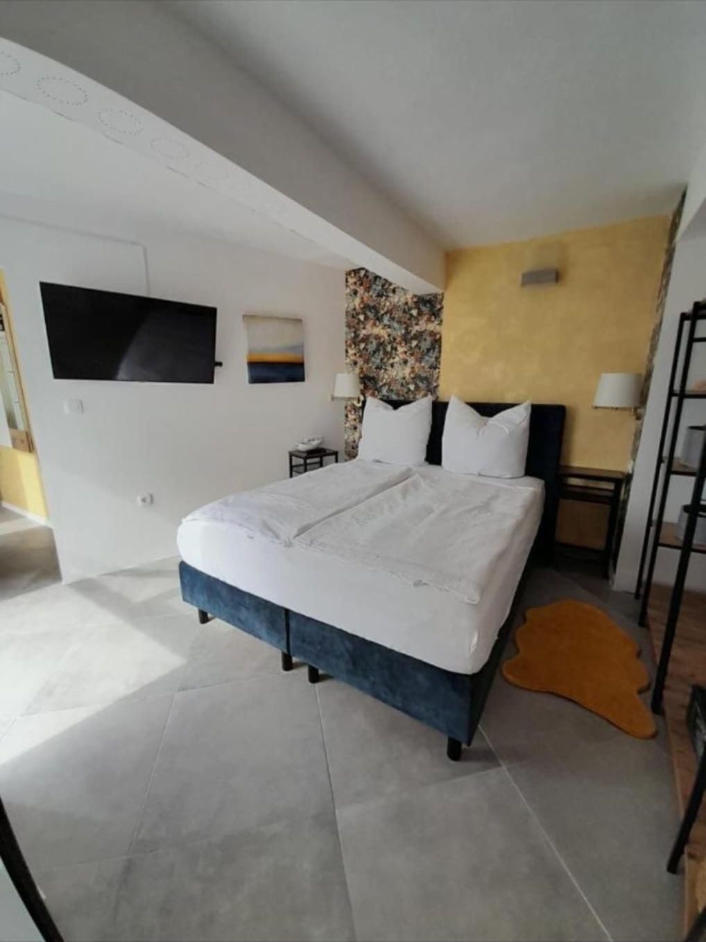 Schlafzimmer mit blauem Boxspringbett und Smart-TV